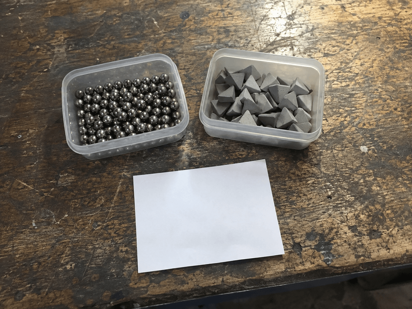 AI illustration of generic steel balls and ceramic media in two trays on a worn workshop bench.