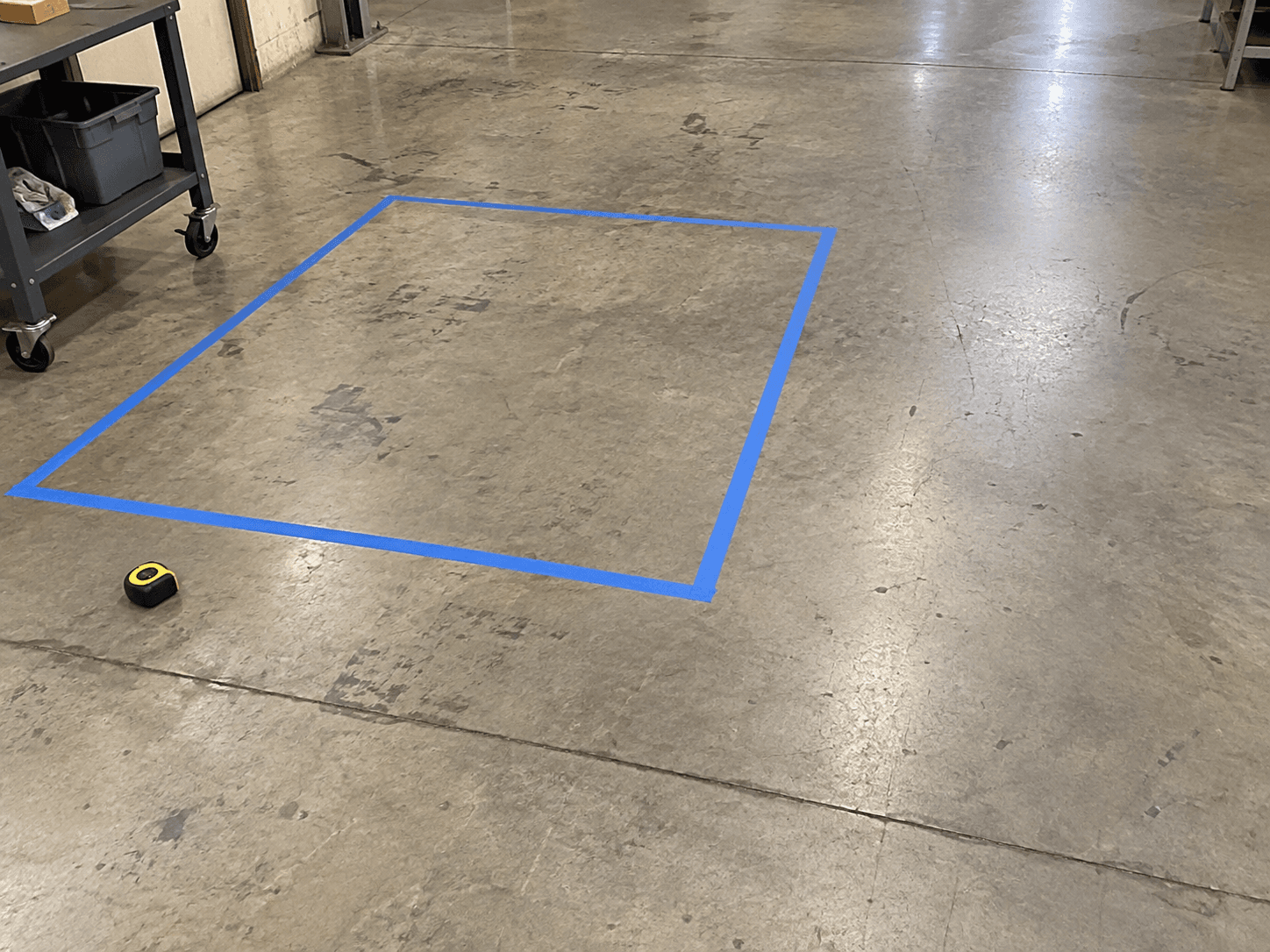 AI illustration of an empty workshop floor marked with a blue tape rectangle beside an aisle.