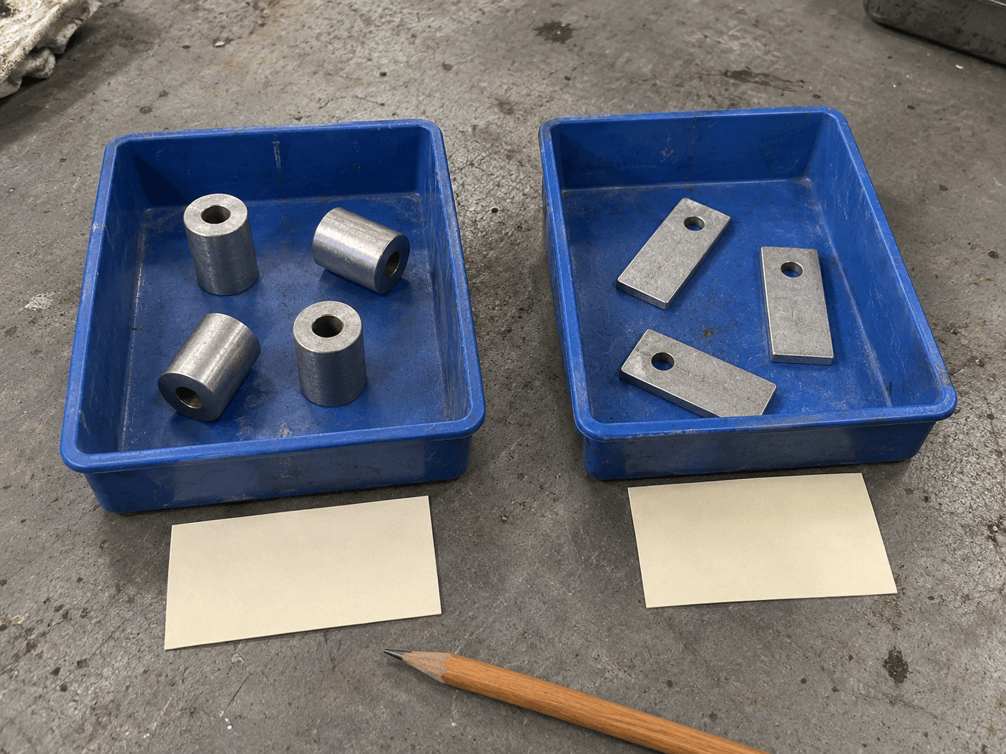 AI illustration of cylindrical spacers and flat metal tabs in separate blue trays on a worn workshop bench.