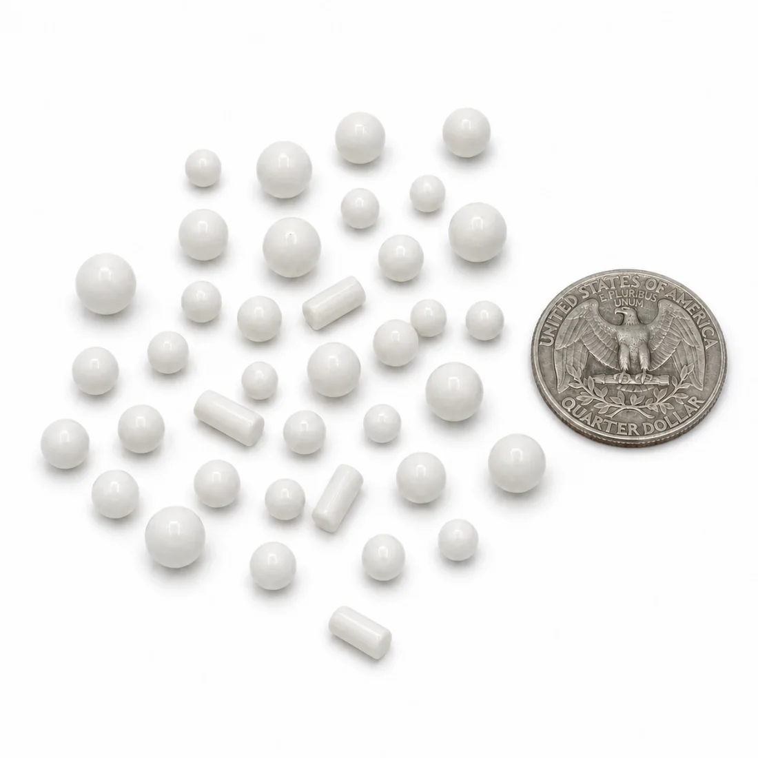 Glossy white spheres and short cylinders scattered beside a US quarter