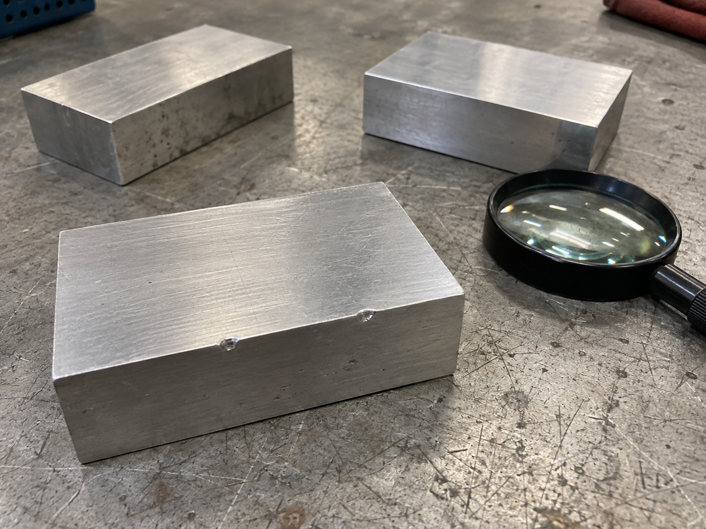 AI illustration of aluminum blocks with small edge dings beside a magnifier on an inspection bench.
